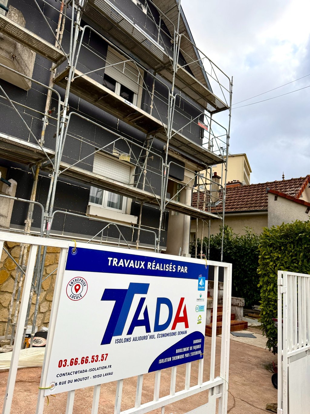 Chantier pose isolant sur façade avec échafaudage et pancarte TADA 