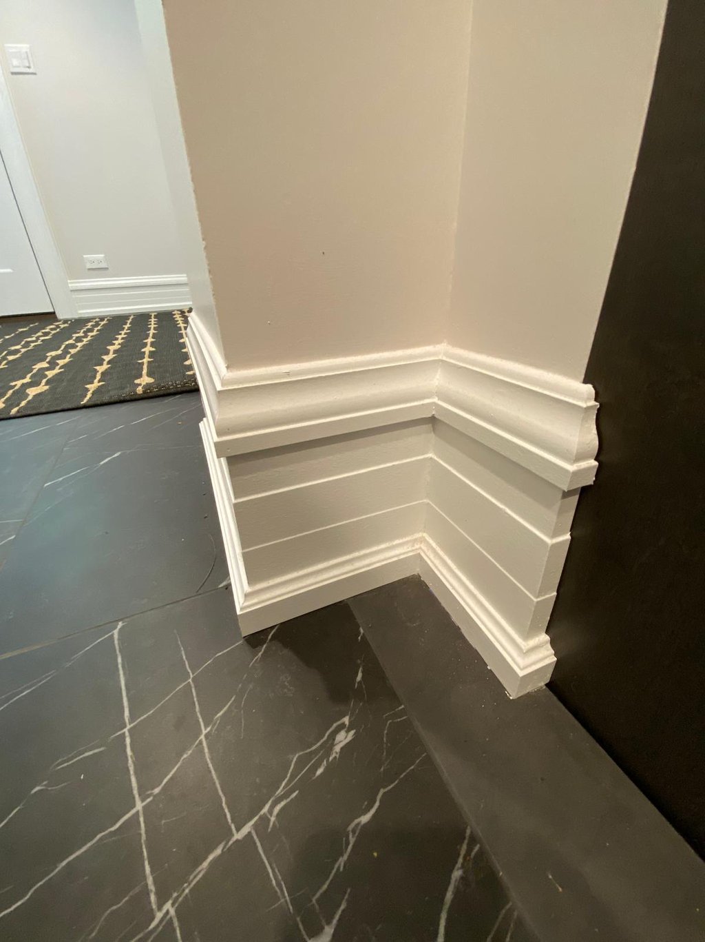 Elegant white baseboard and decorative wall trim installed above black marble floor tiles.