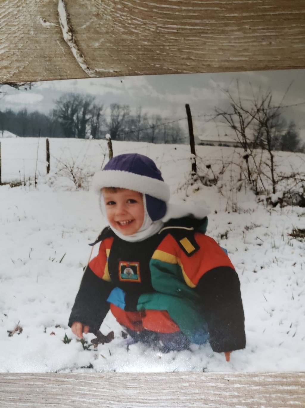 Monsieur rêve enfant, vêtu d'une veste d'hiver colorée et d'un bonnet violet, joue dans un champ