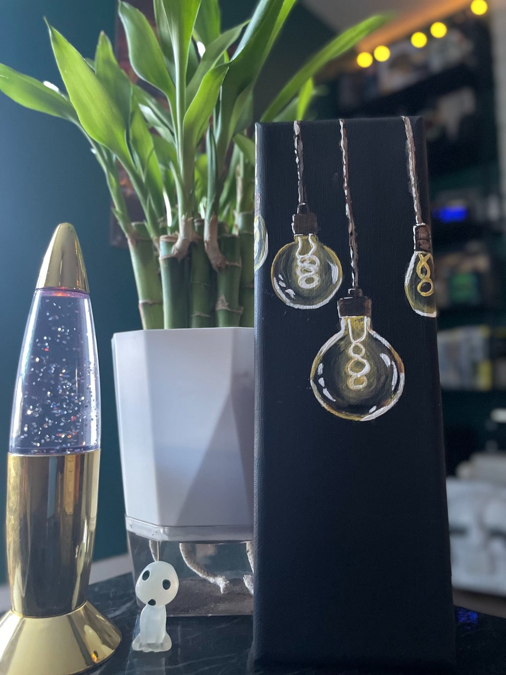 painting of lightbulbs on table with lava lamp and lucky bamboo plant