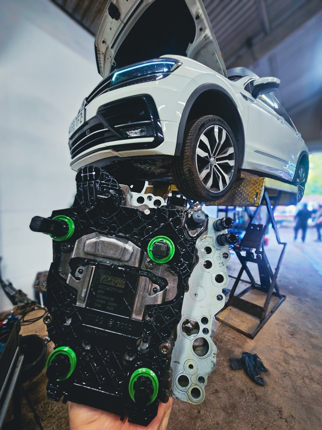 A white Volkswagen Tiguan on a hydraulic lift in a repair shop with a DQ381 mechatronic unit