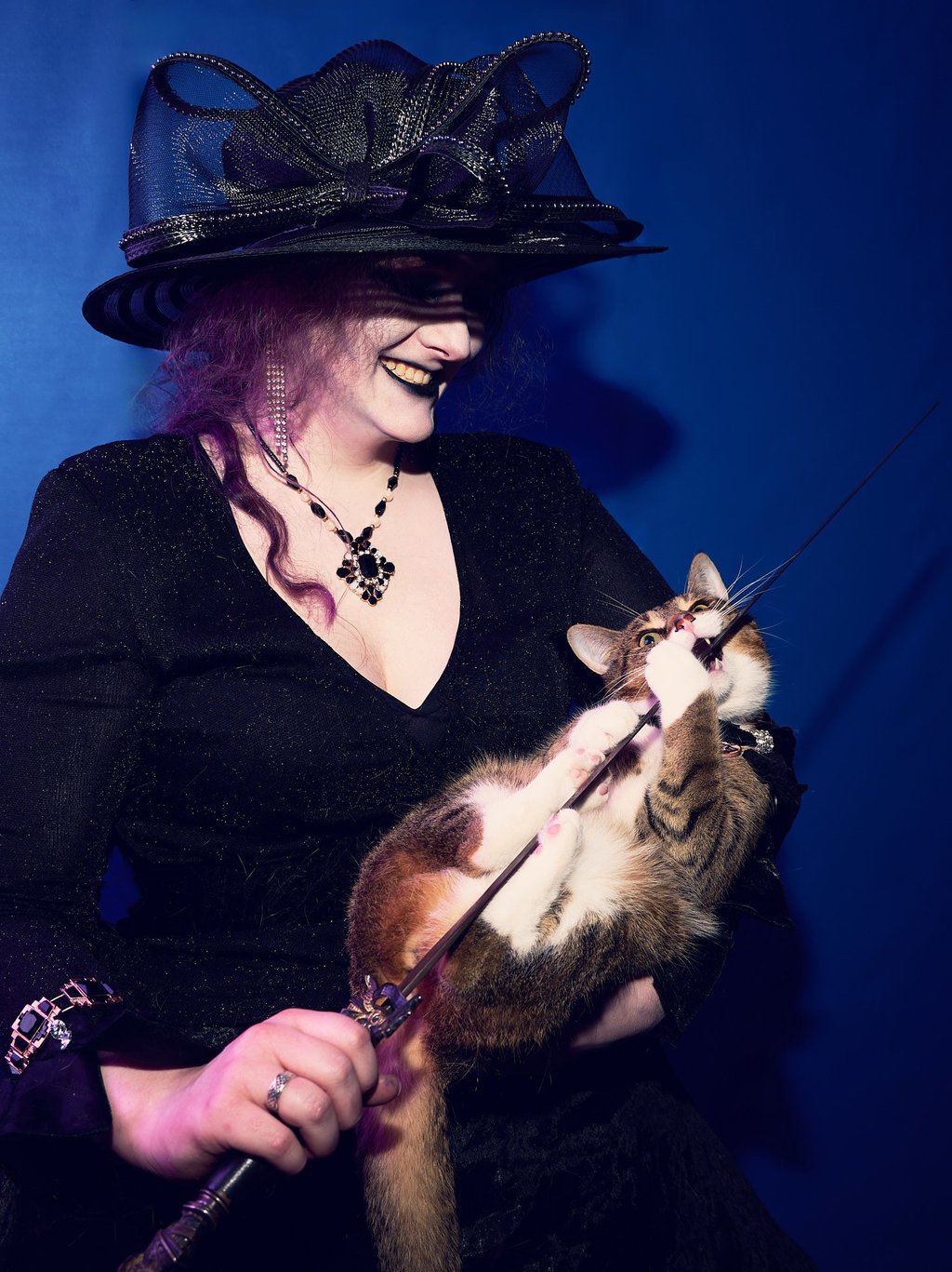 a woman in a black hat holding a cat which is biting a sword