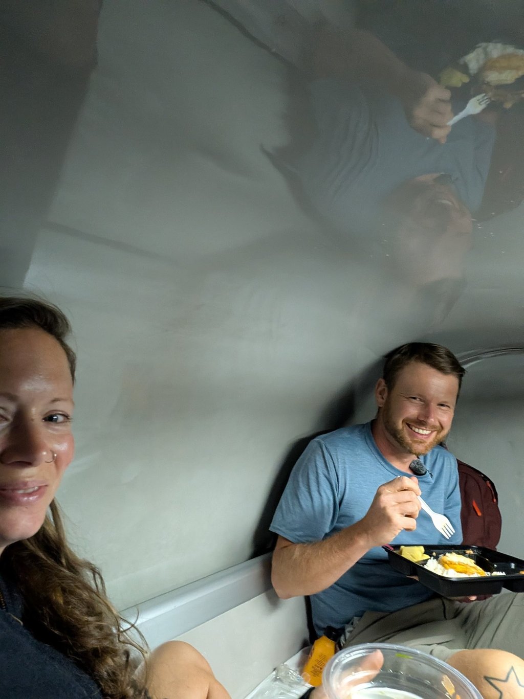 don and Samantha eating a meal inside a small train cabin while traveling.