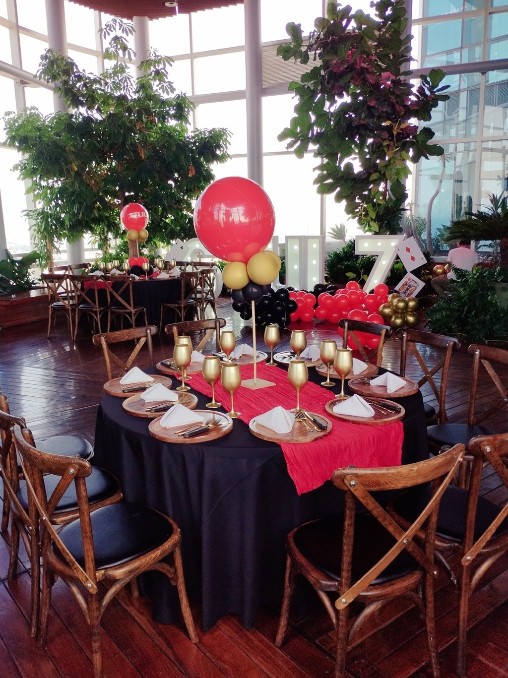 Elegant casino themed party table setting with gold goblets, red runner, and balloon centerpieces.