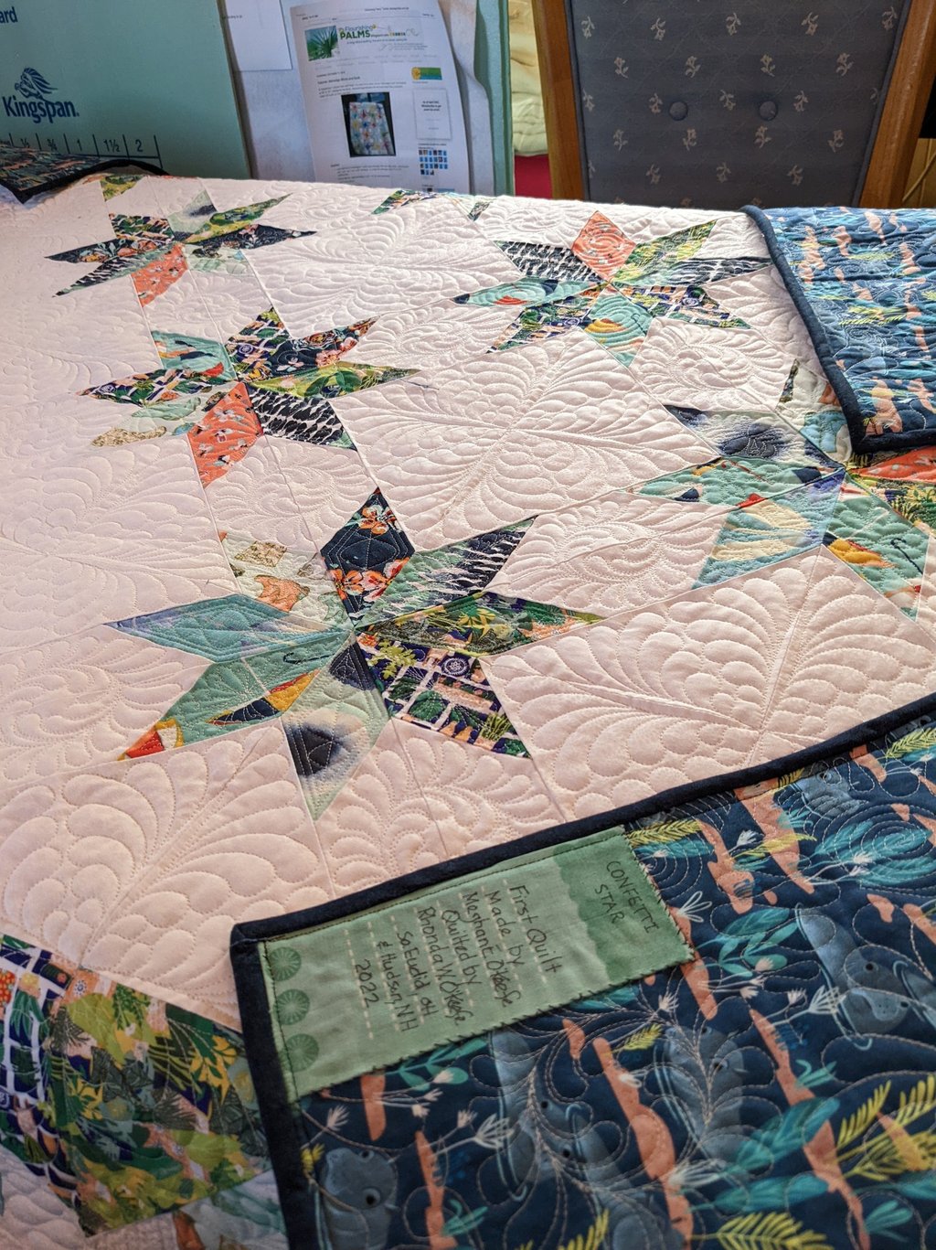 a white quilt with colorful stars and ornate quilting and a hand-lettered label