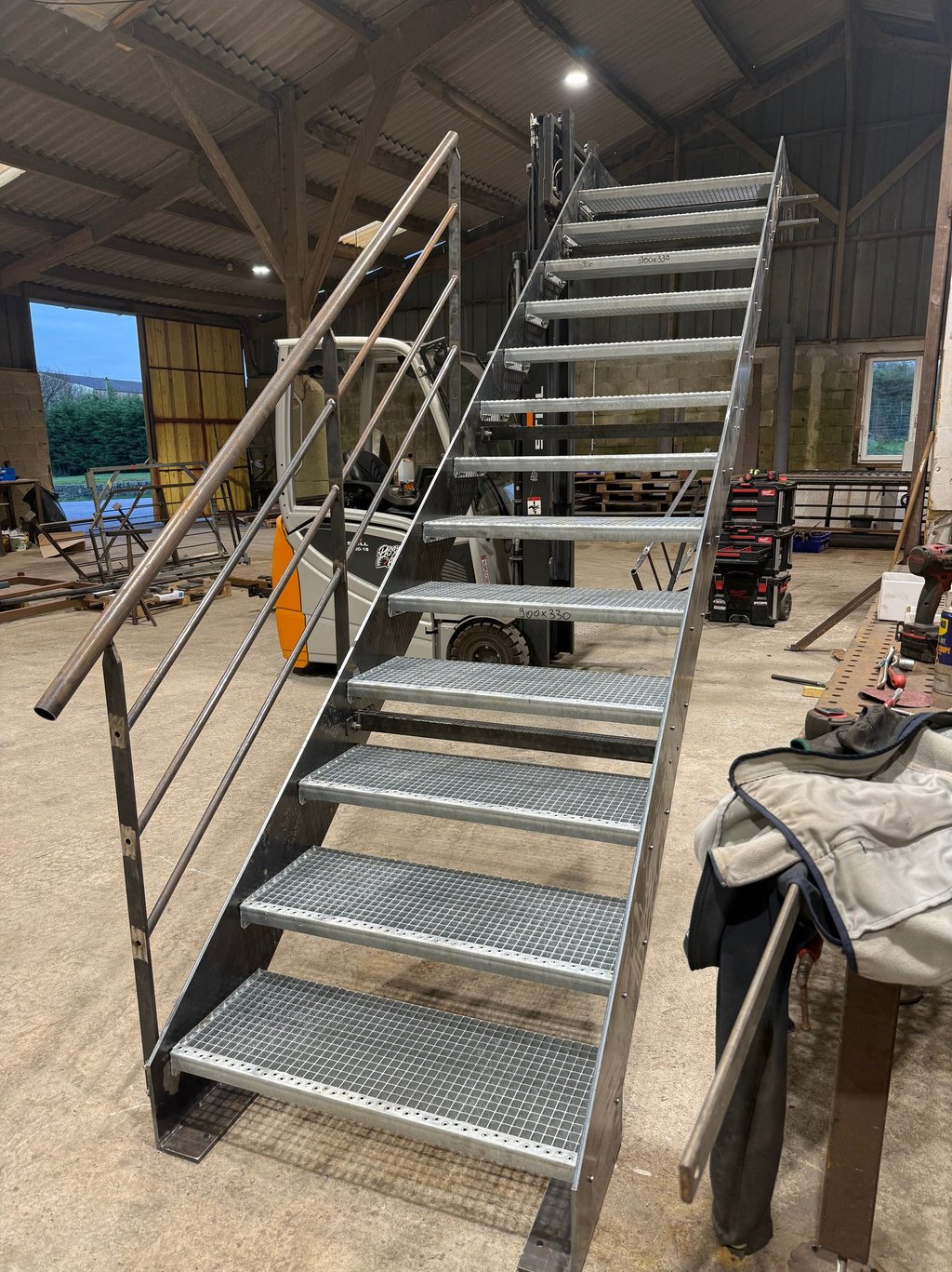 Industrial galvanized steel staircase with non-slip grating treads and metal handrails in a workshop.