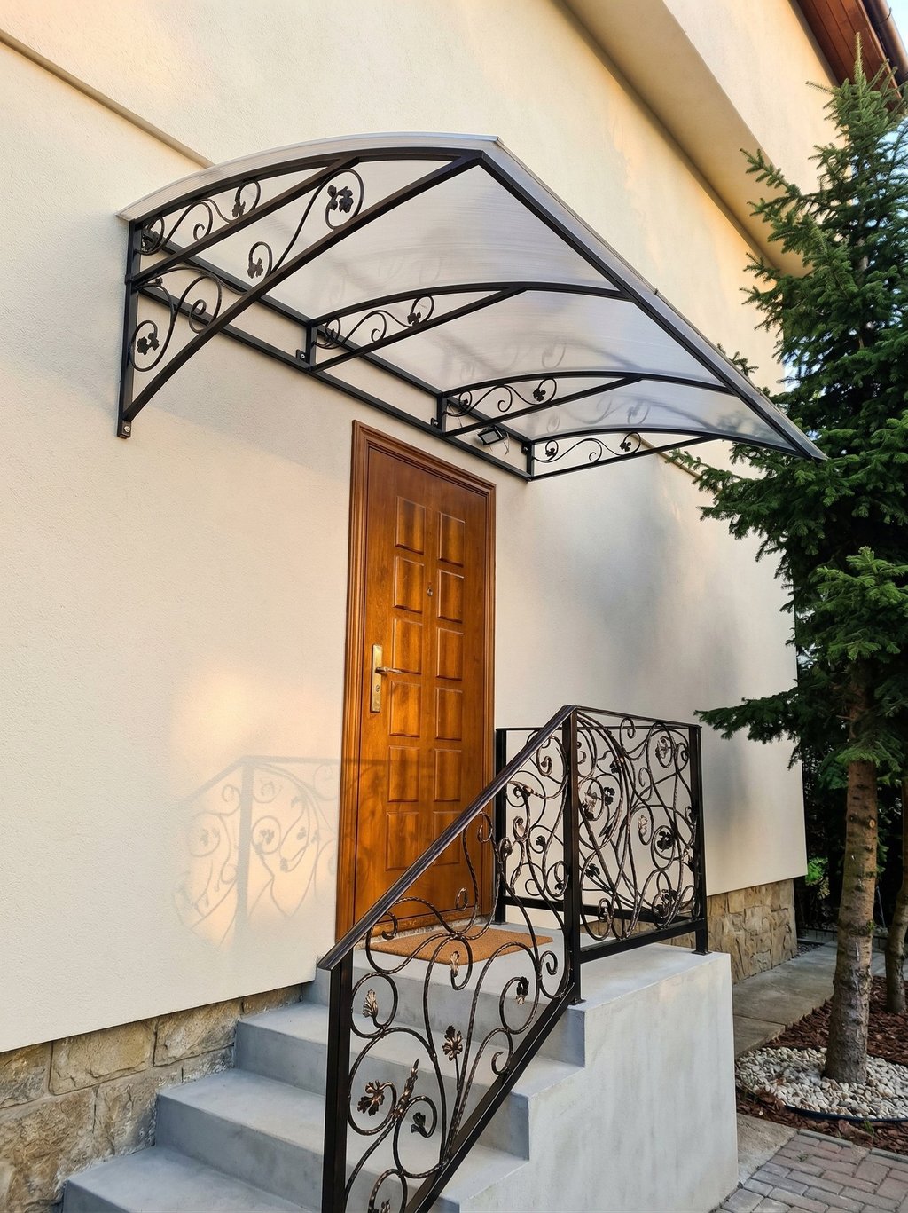 Elegant wrought iron door canopy with polycarbonate roof over a wooden entrance door and matching railing.