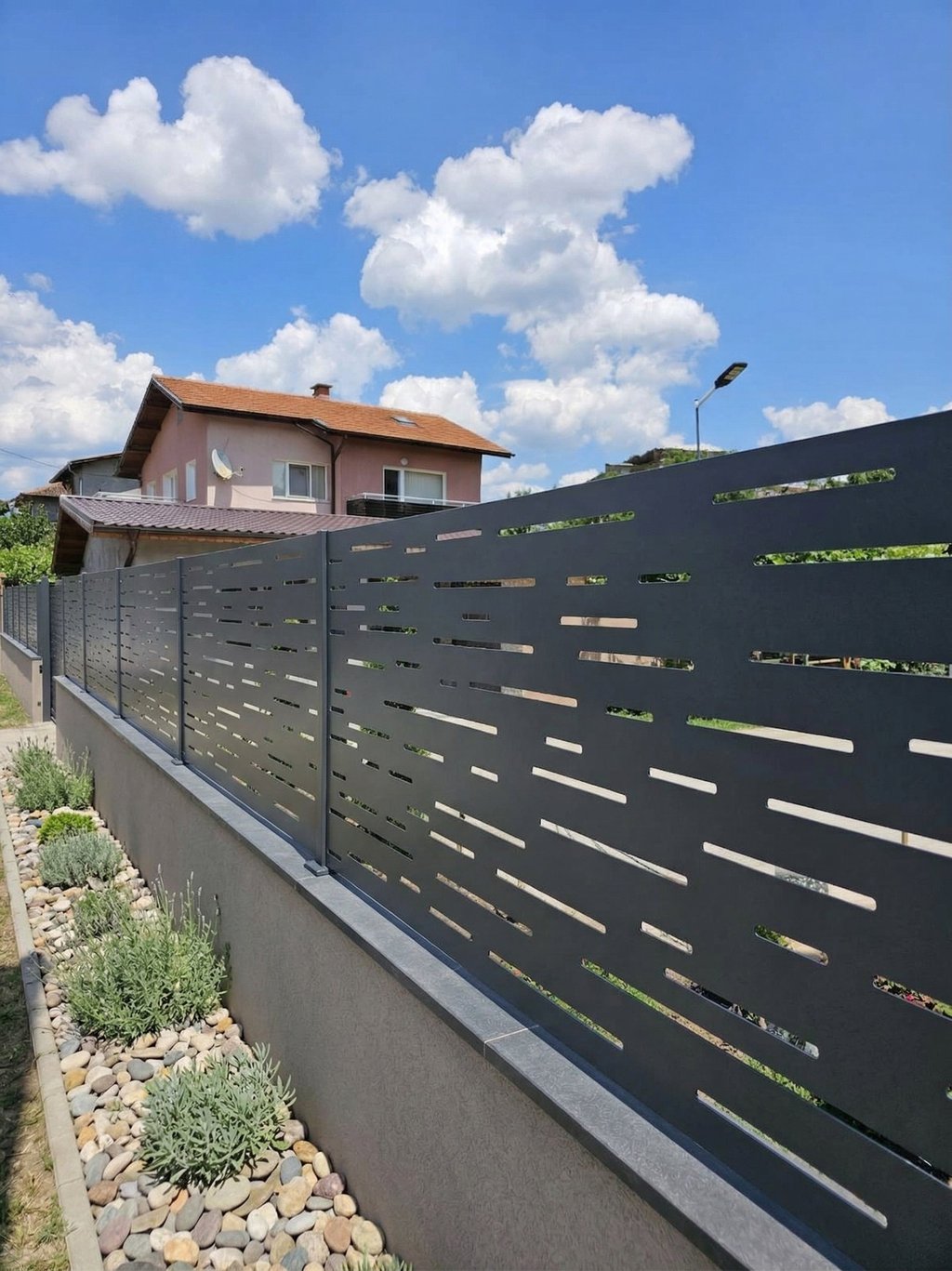 Modern anthracite laser-cut metal privacy fence installed on a concrete wall in a residential garden.