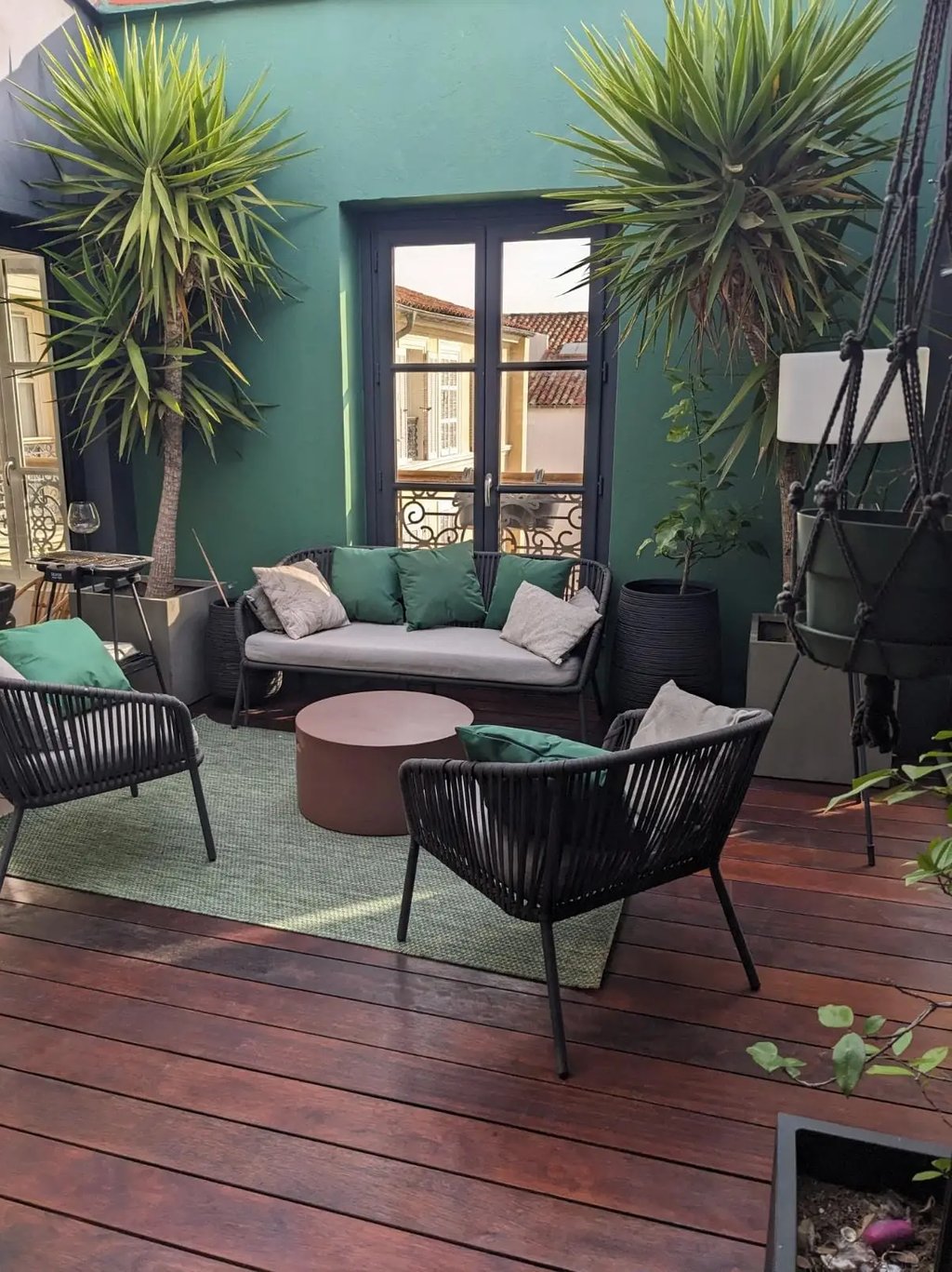 Aménagement d'une terrasse avec salon de jardin, terrasse bois rouge et mur vert décoratif. Harenova