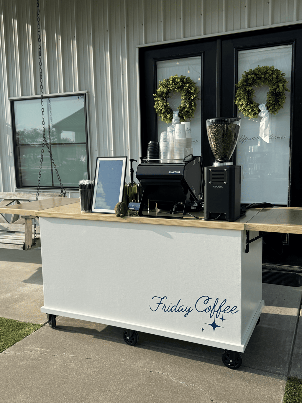 Mobile espresso bar setup with an espresso machine and coffee bean grinder on a white cart.