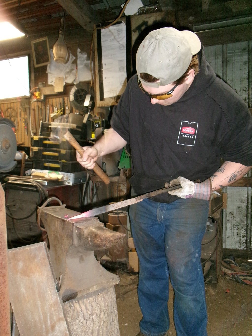 A blacksmith in a workshop uses a hammer to shape glowing hot metal on an iron anvil.