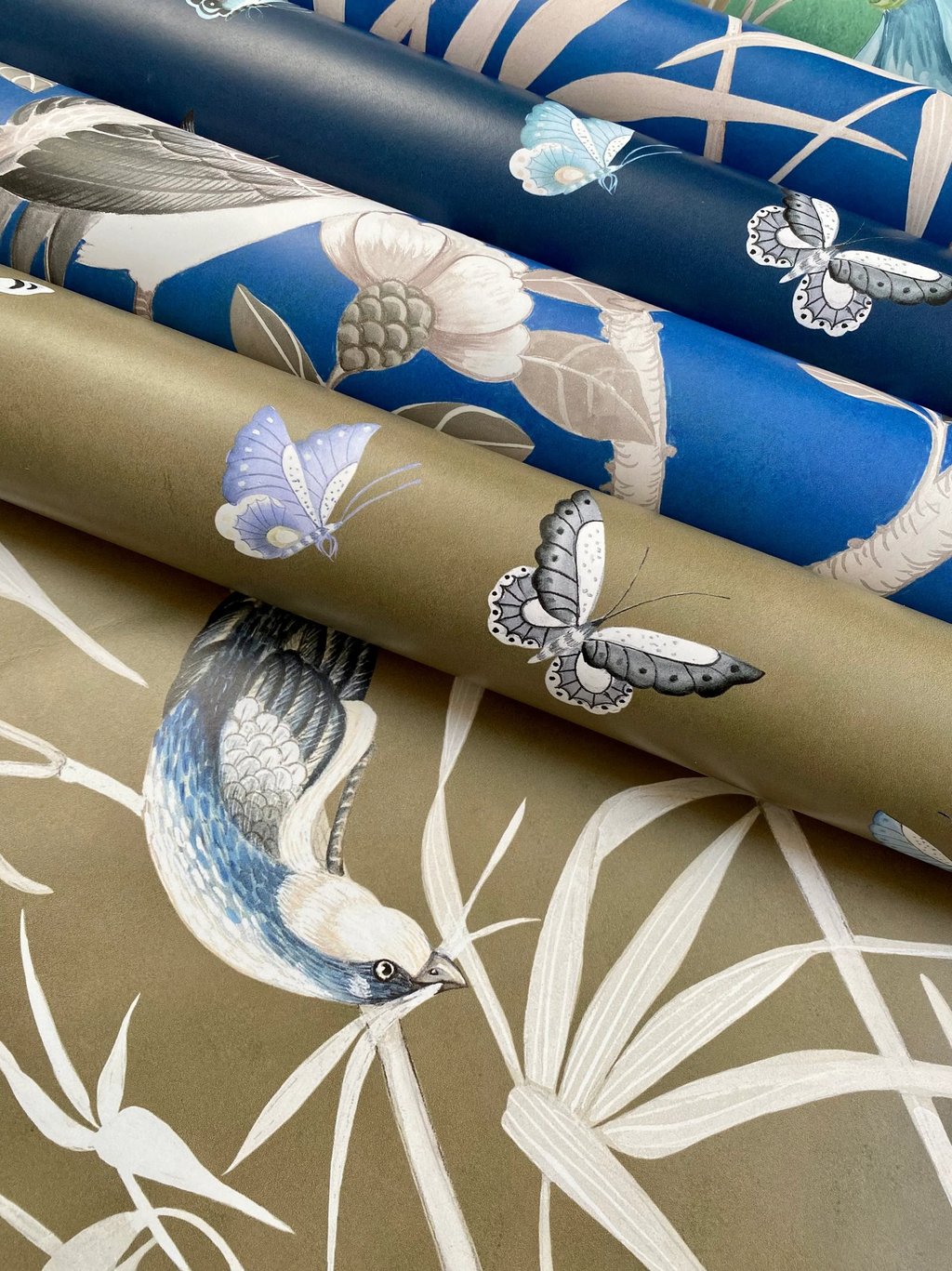 Rolls of luxury designer wallpaper featuring bird and butterfly motifs in blue and gold colors.