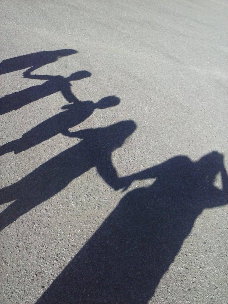 Shadows of a group of people holding hands on a gray pavement surface to represent unity and teamwork.