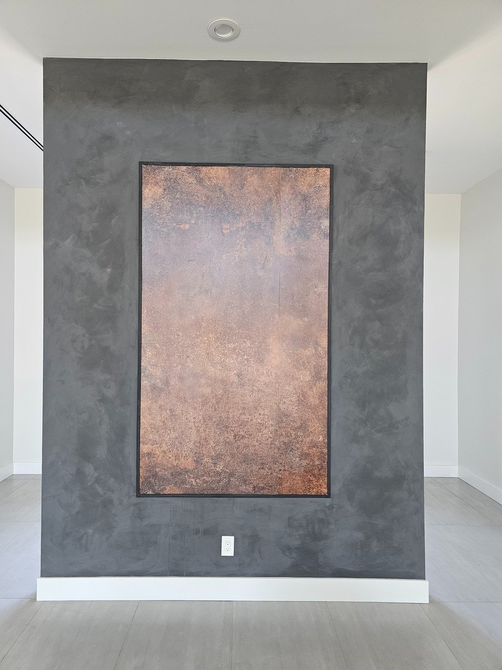 Bold black limewash wall with a rectangular copper wallpaper inset, combining textured depth with warm metallic contrast 