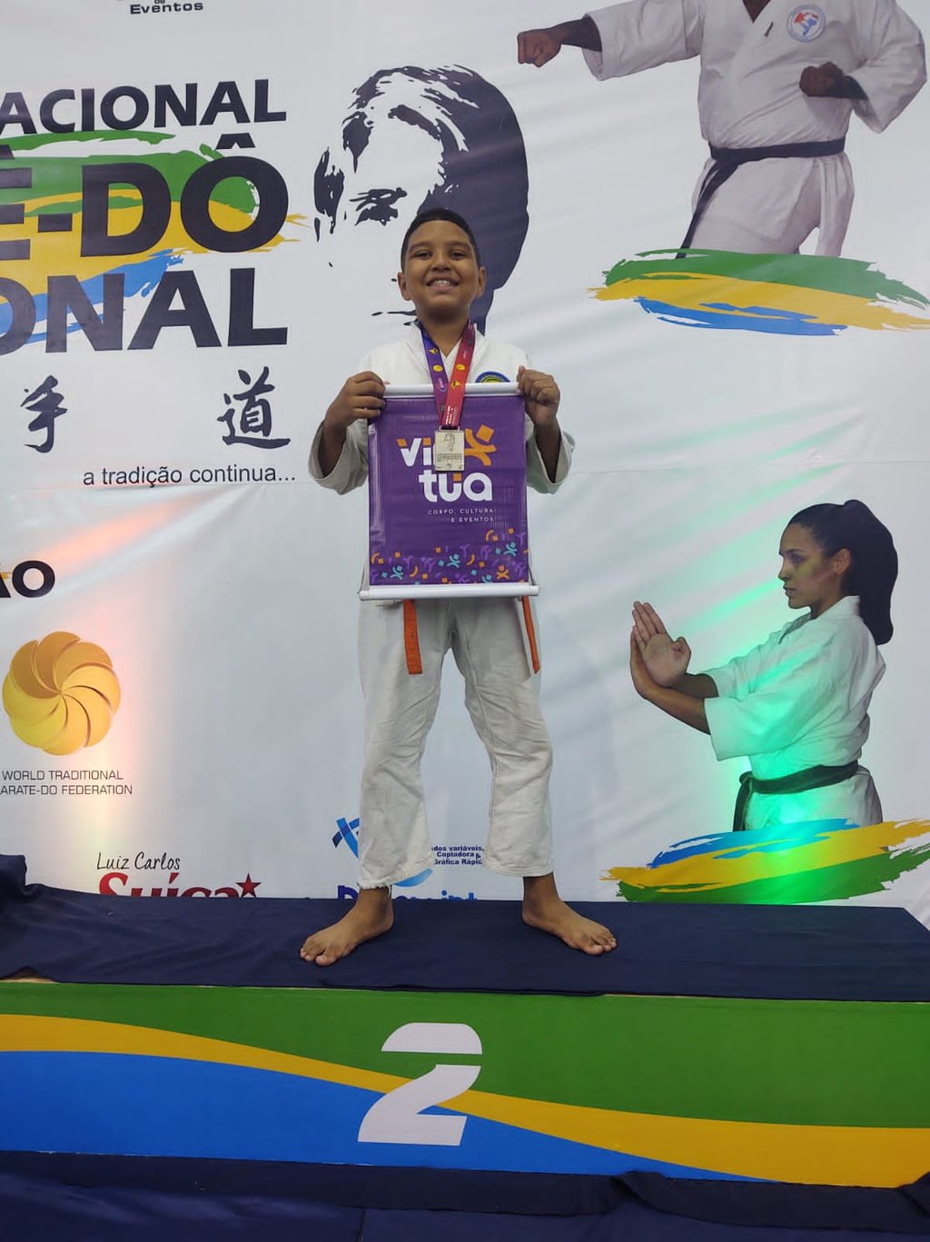 Young karate athlete with a medal standing on a podium at a martial arts championship event.