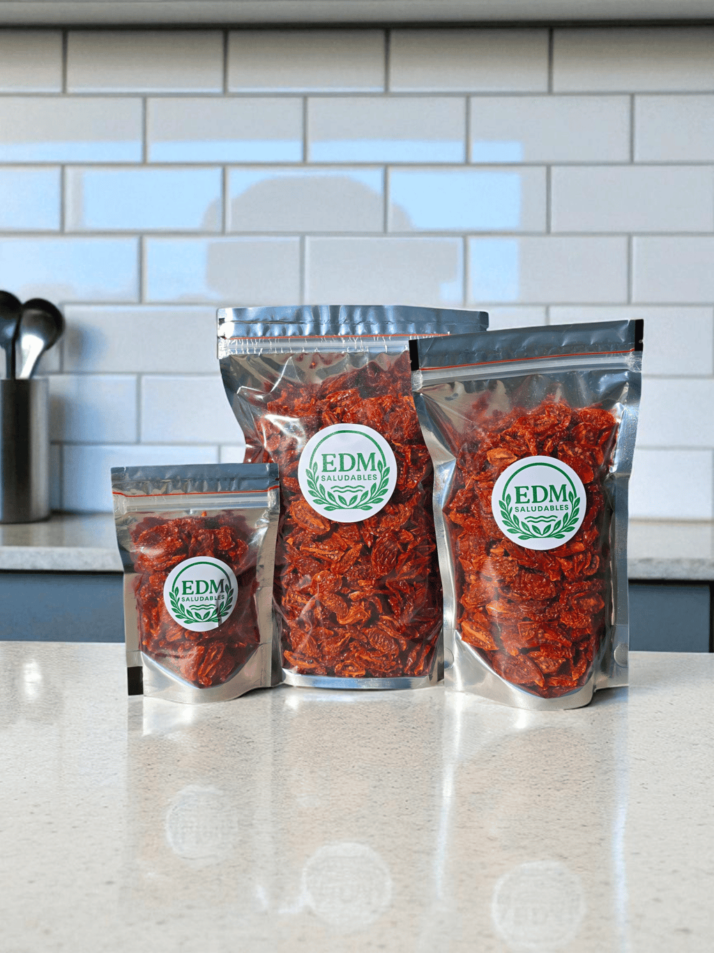 Tres tamaños de envases con tomates cherry deshidratados, sobre mesada de mármol.