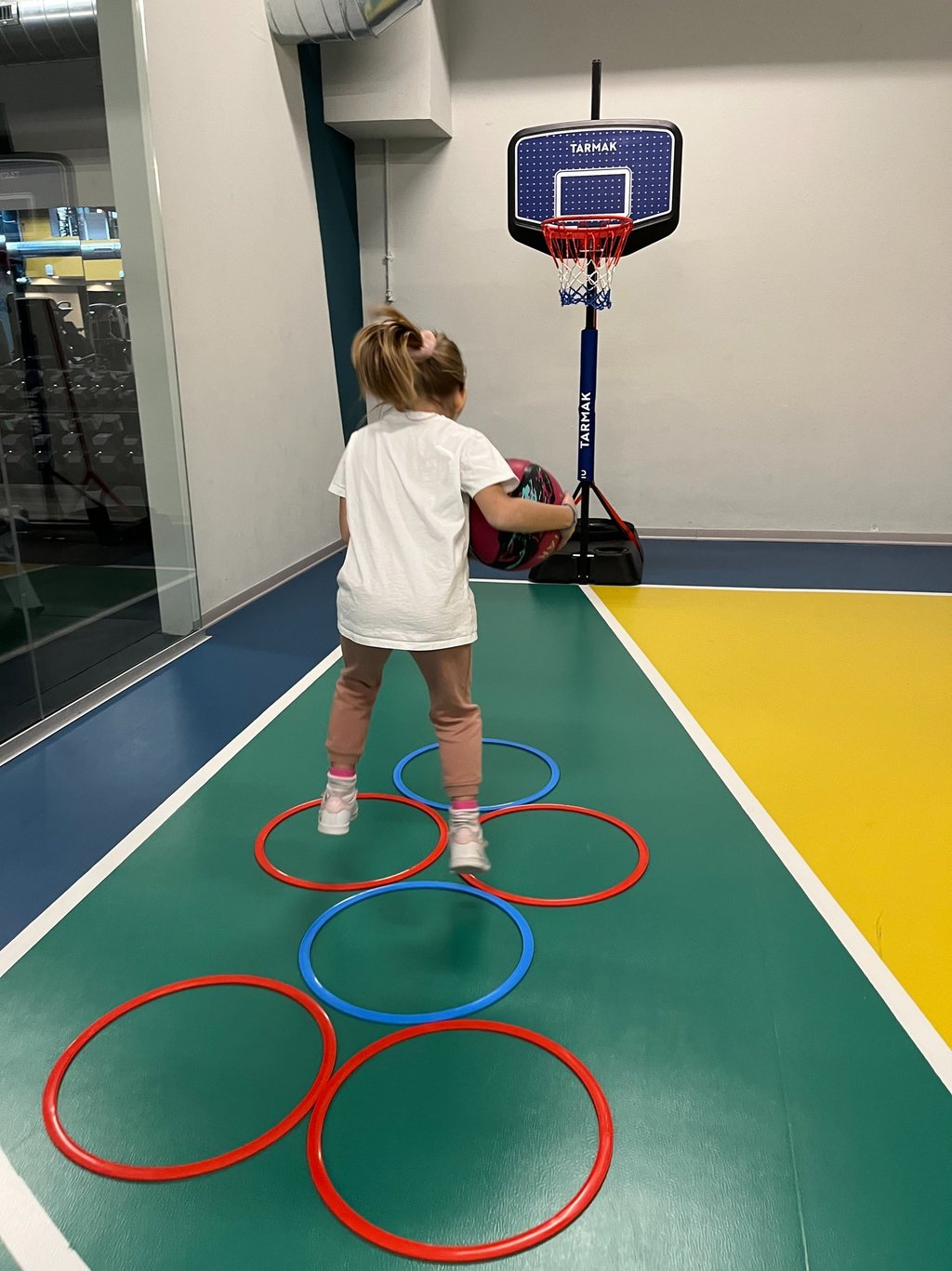 Bambina che gioca con un pallone su un campo multisport nella palestra Move 2 Grow a Milano, utilizzando cerchi colorati 