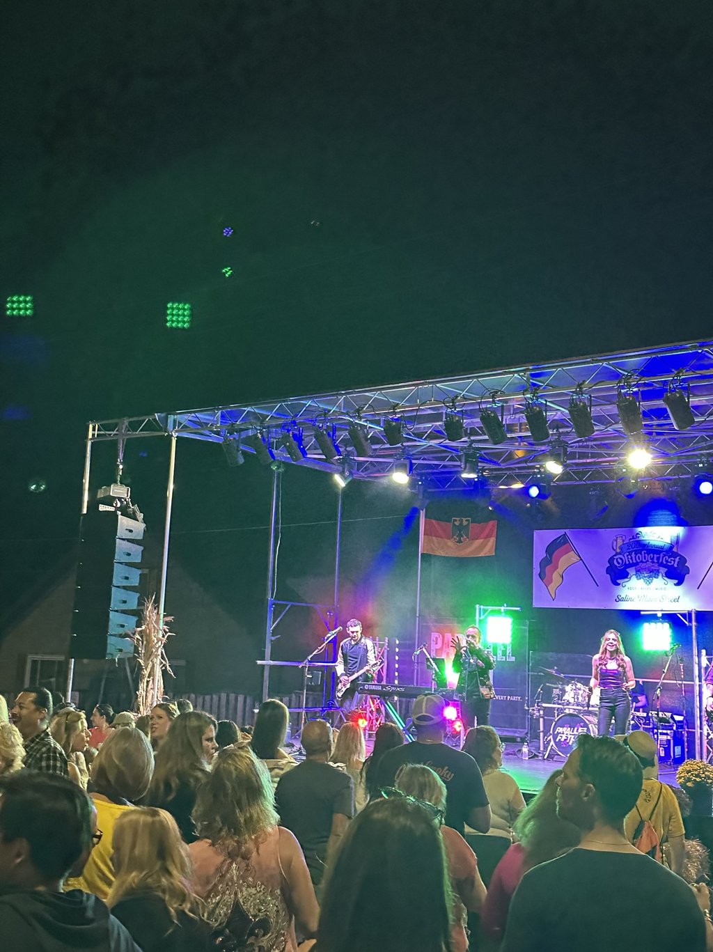 Live band performing on an outdoor stage at an Oktoberfest festival with a cheering crowd.