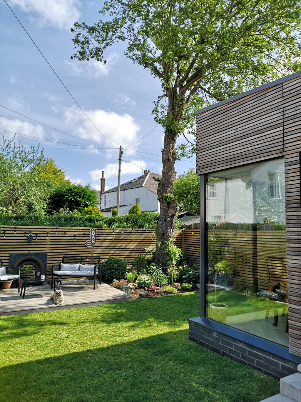Modern garden design featuring a timber-clad garden room, wooden slatted fence, and a sunny lawn area.