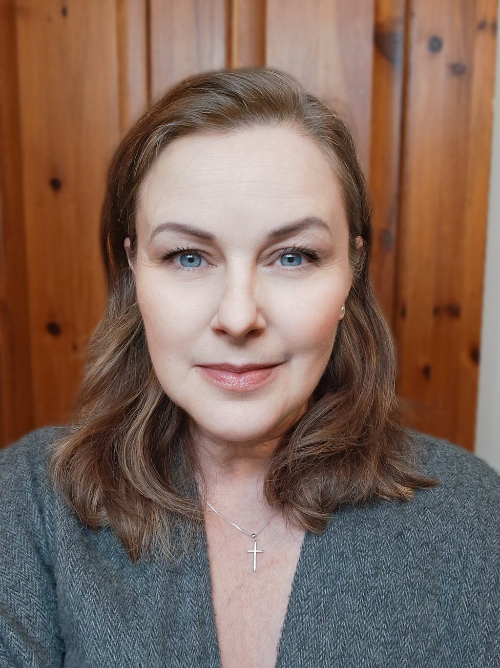 Professional headshot of a woman with blue eyes and brown hair wearing a silver cross necklace.