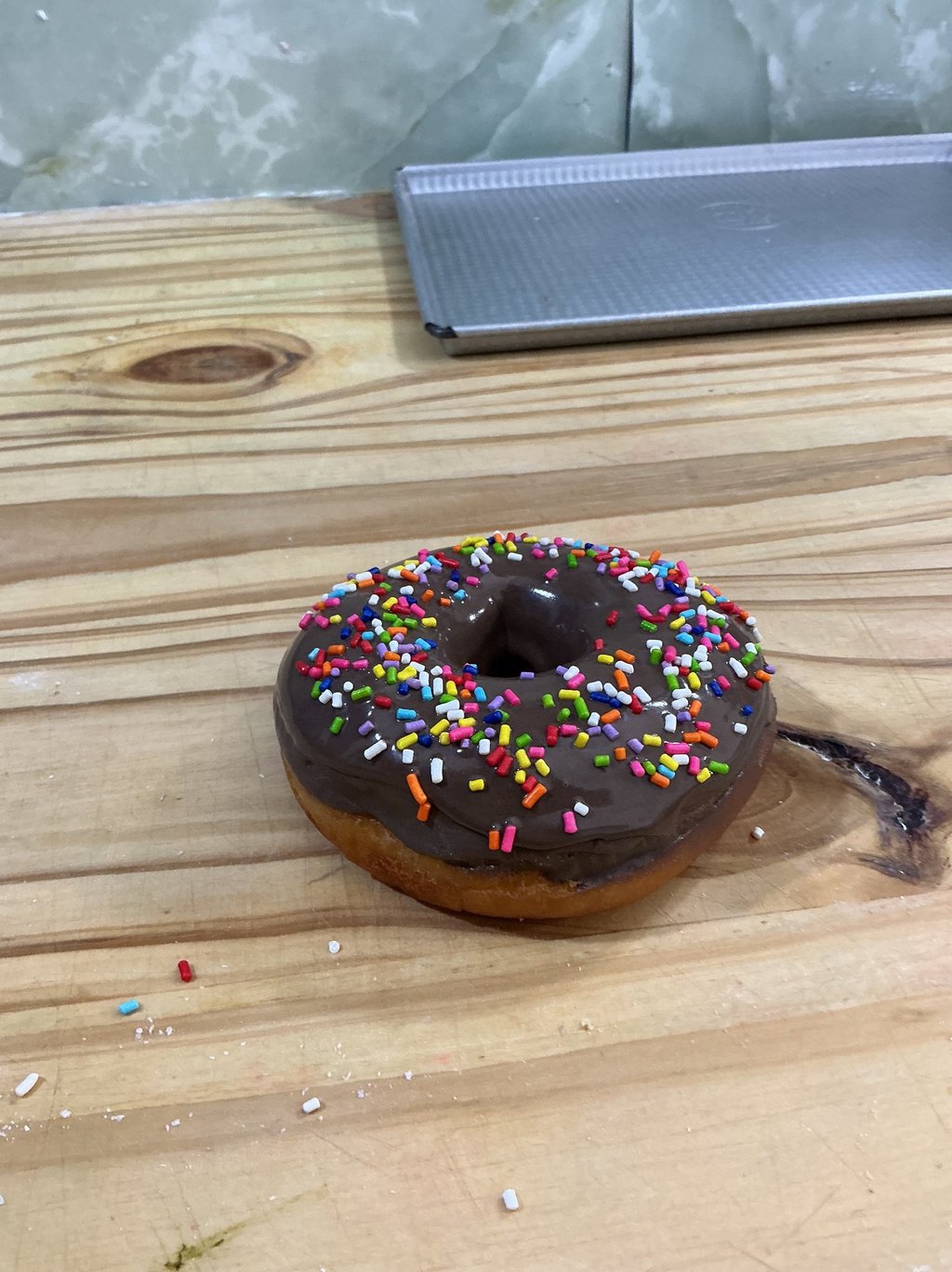 Donut glaseado de chocolate recién horneado con coloridas chispas de arco iris sobre una mesa de mad