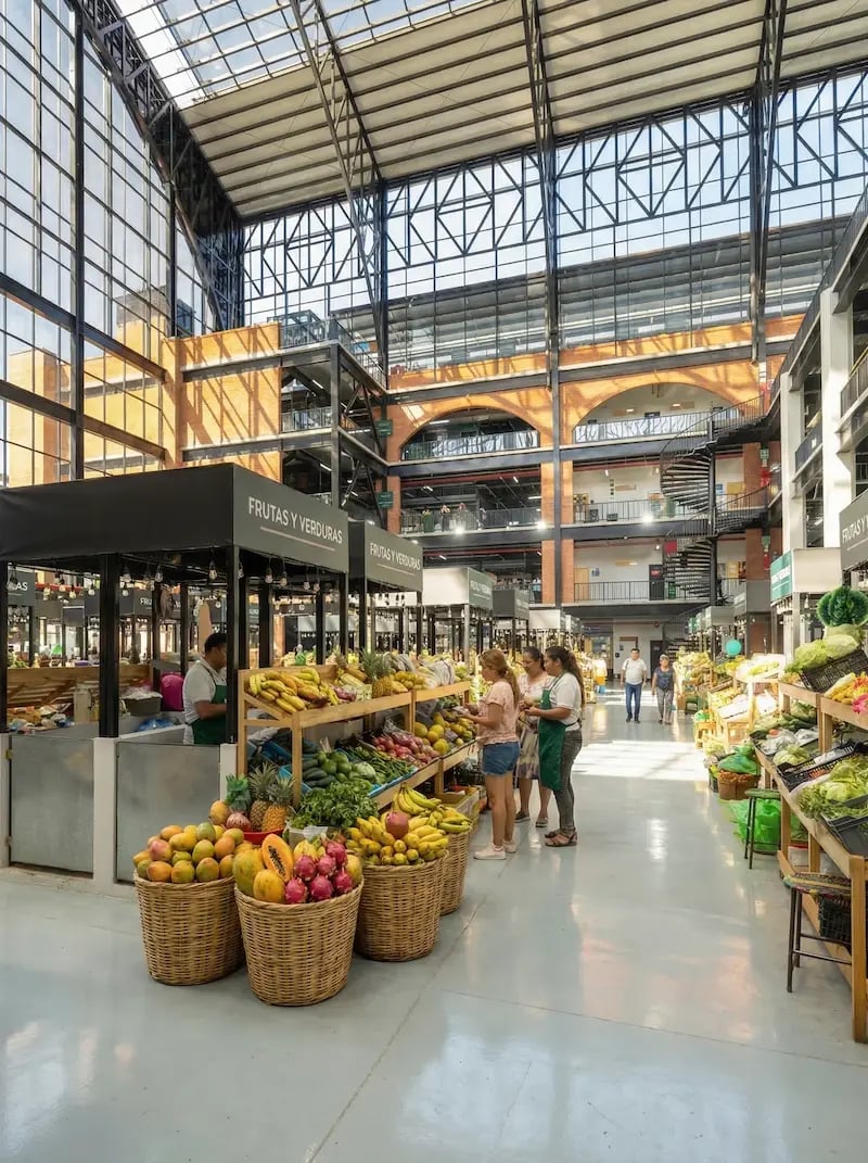 Customers shopping for fresh tropical fruit at a modern indoor market with glass ceilings.