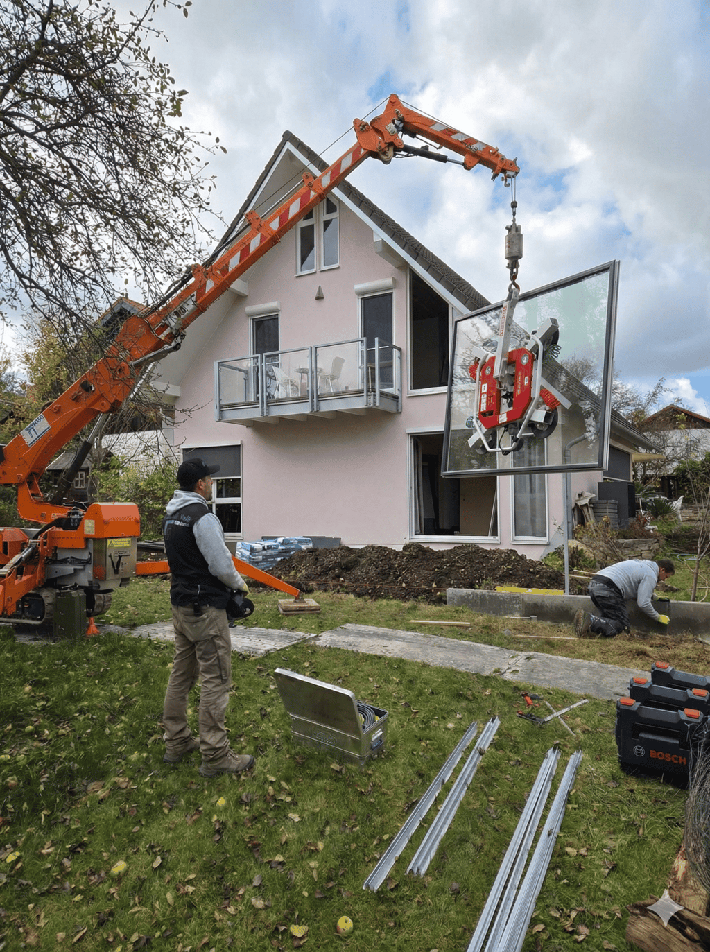 Oranger Minikran hebt mit einem Saugheber eine große Glasscheibe zur Montage in das Obergeschoss eines Wohnhauses.