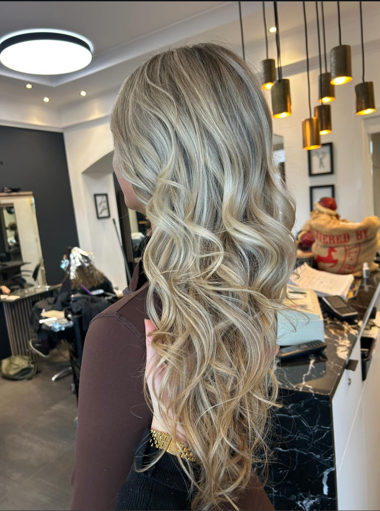 Woman with long blonde balayage hair featuring loose waves and highlights styled in a professional hair salon.