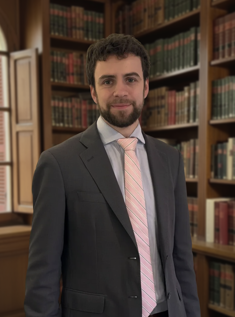 Lawyer in a suit and pink tie posing in a traditional library with law books.