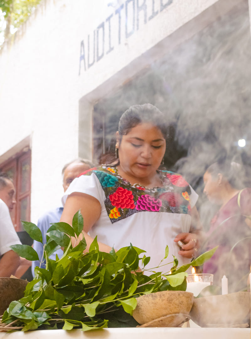 Una mujer con una blusa tradicional mexicana bordada realiza una ceremonia de limpieza con humo 