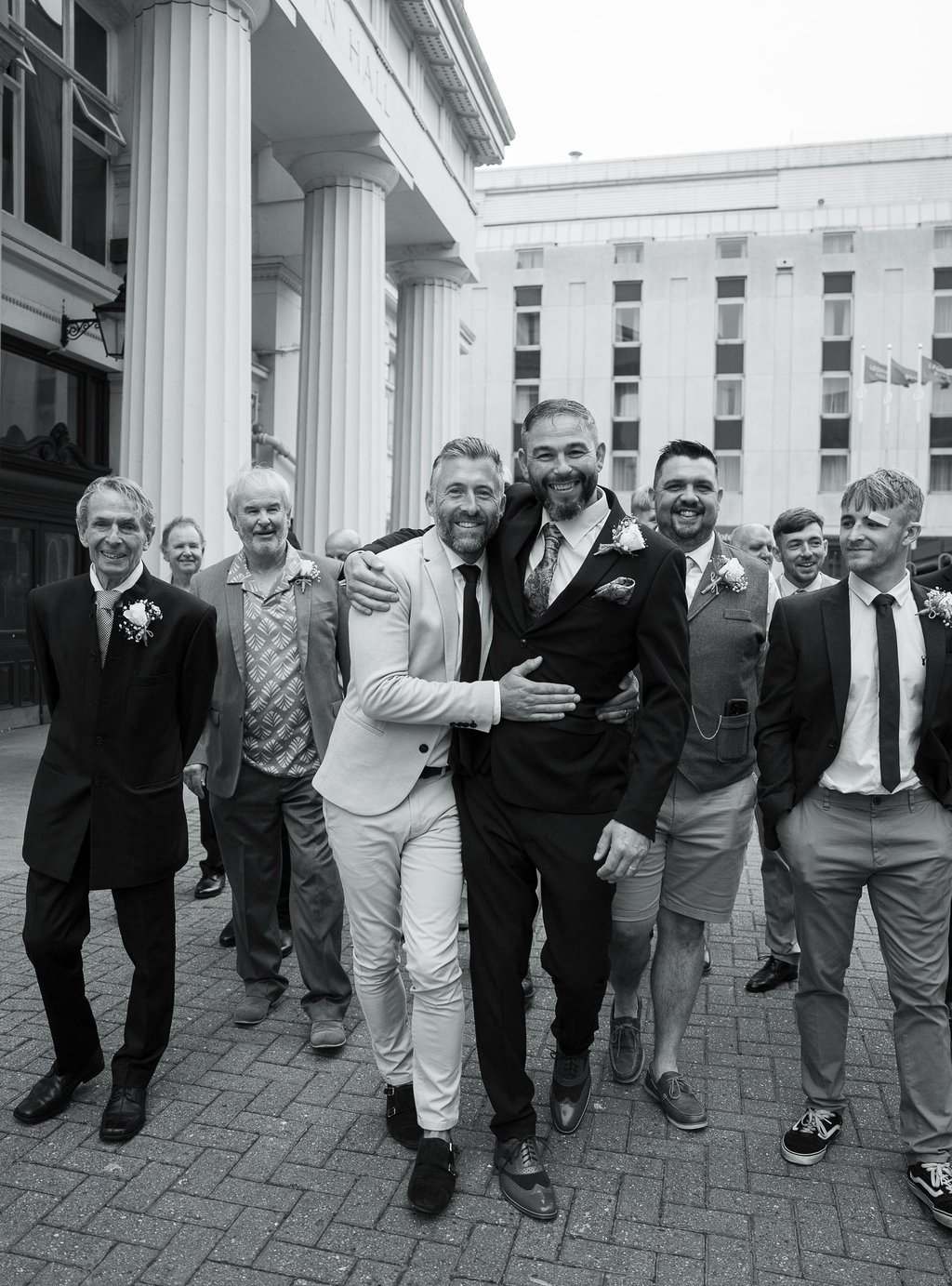 Black and white image of groom with his groomsmen laughing walking 