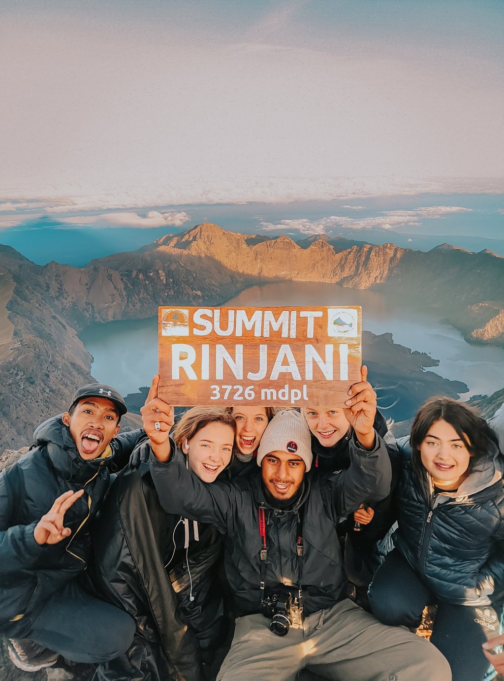 Hikers celebrating at Mount Rinjani summit with crater lake views in Lombok, Indonesia.