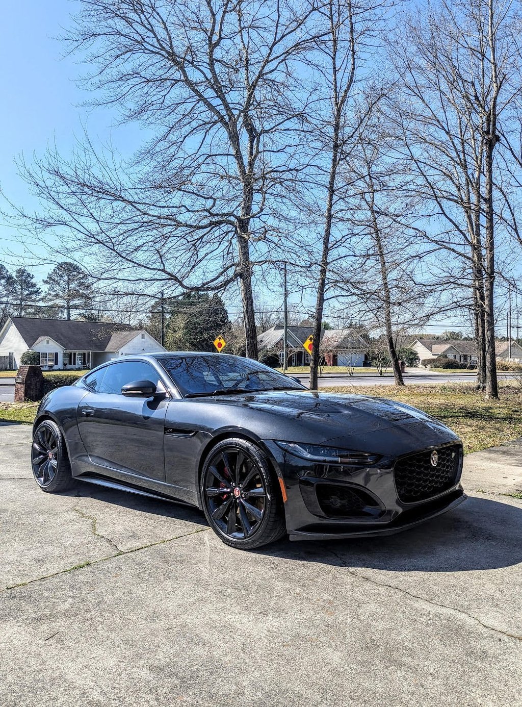 Dark grey Jaguar F-Type luxury sports car parked on a sunny driveway with black wheels.