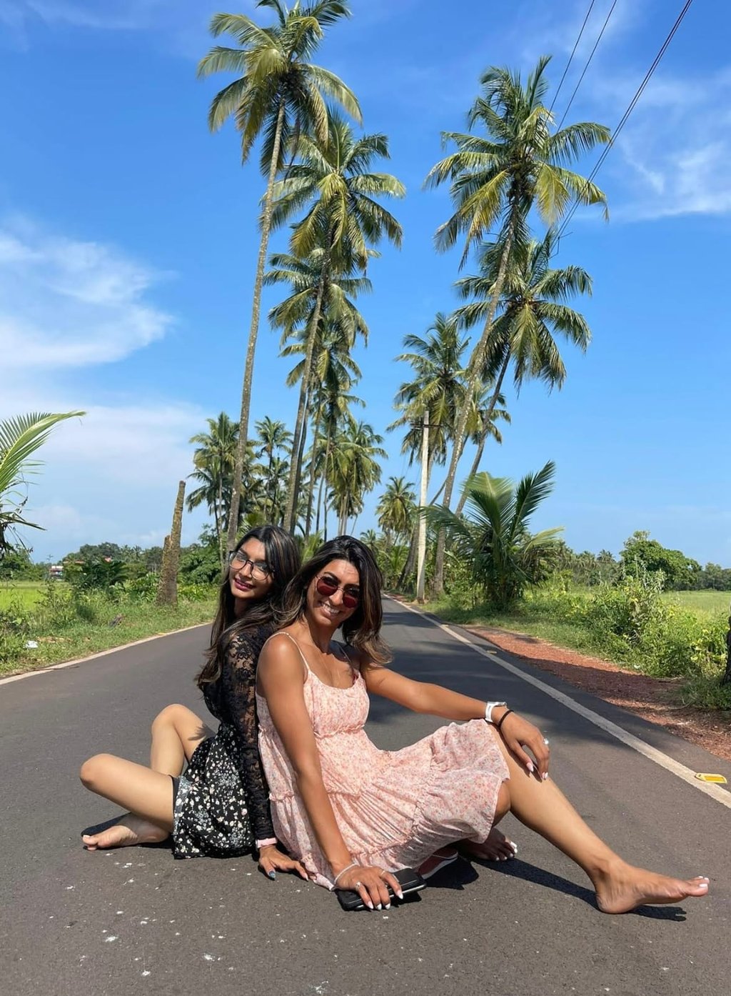 Picture  of 2 sisters siting on the road under Palm trees 