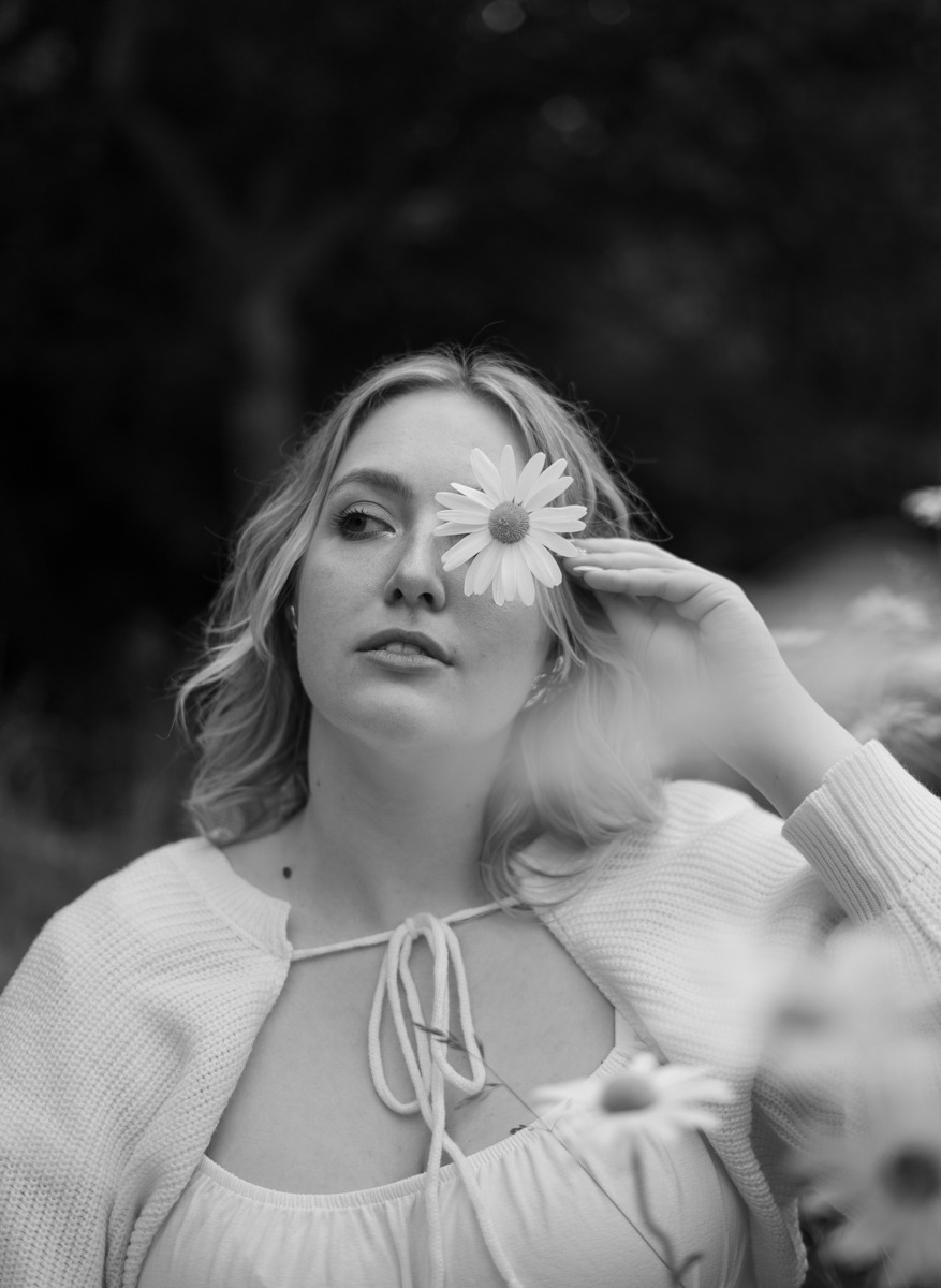 black and white image of woman holding a flower infront of her face