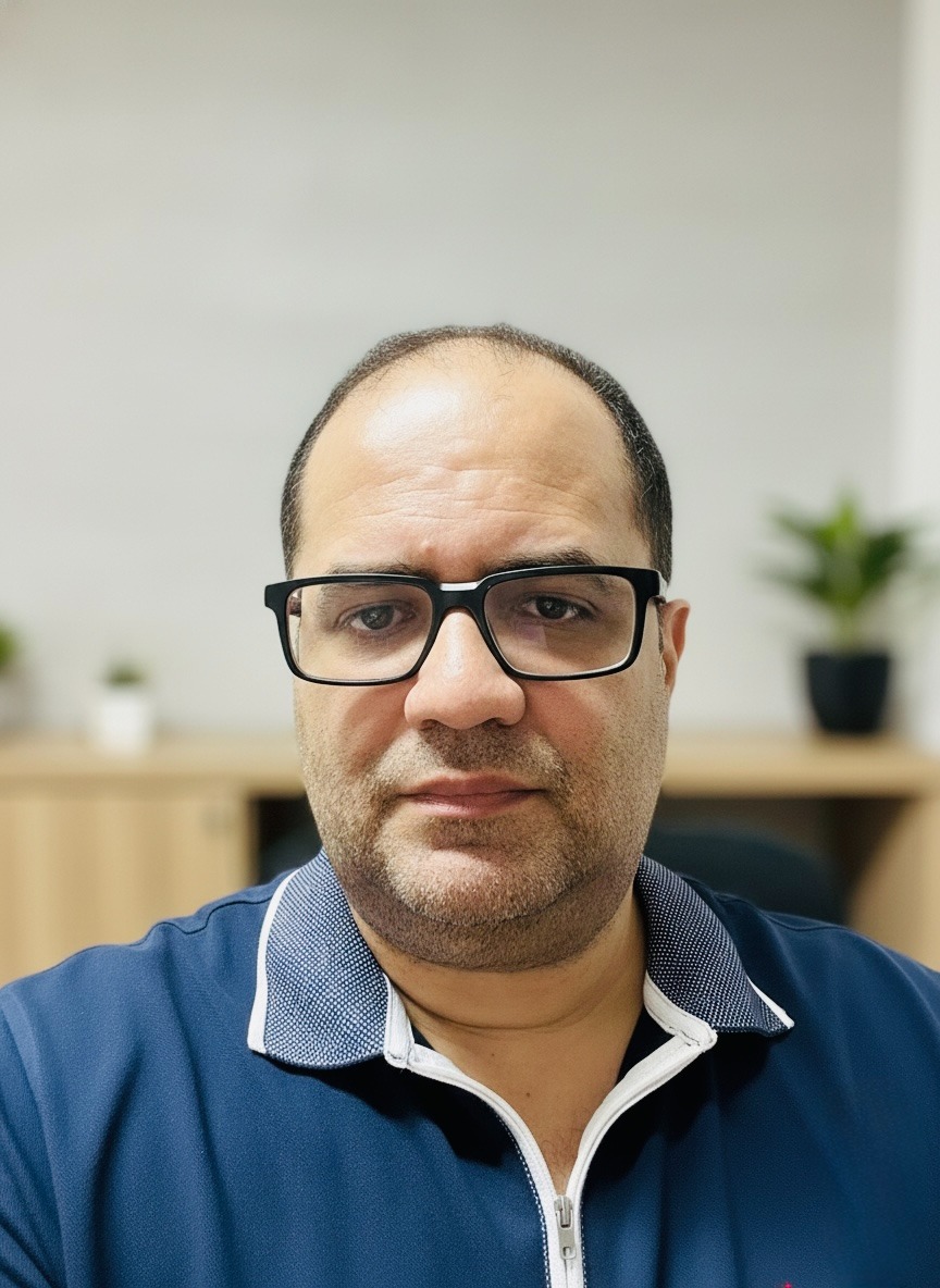 Professional man with black glasses and a blue polo shirt in a bright office setting.
