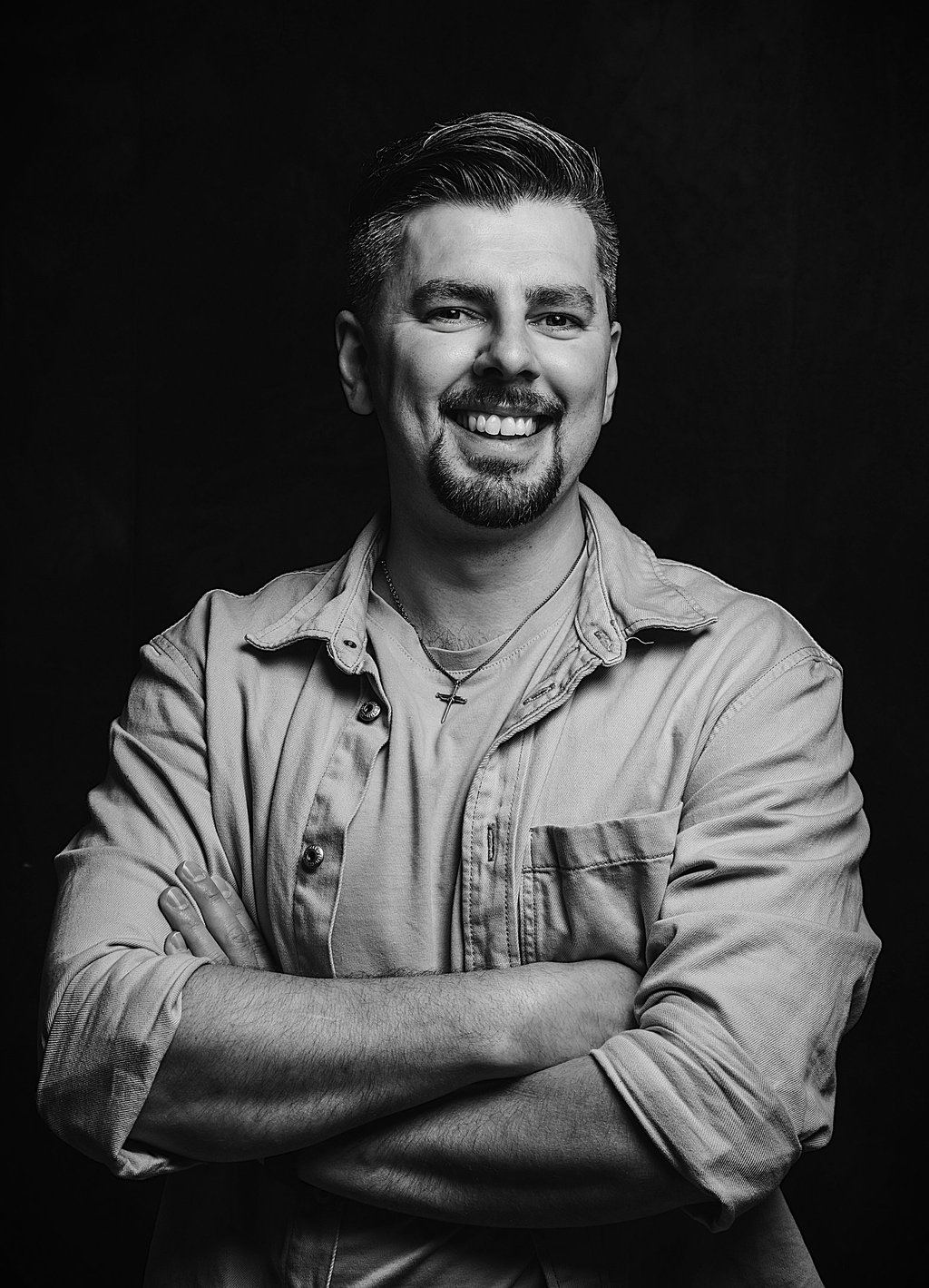 Albert Heit, lächelnd mit verschränkten Armen vor dunklem Hintergrund