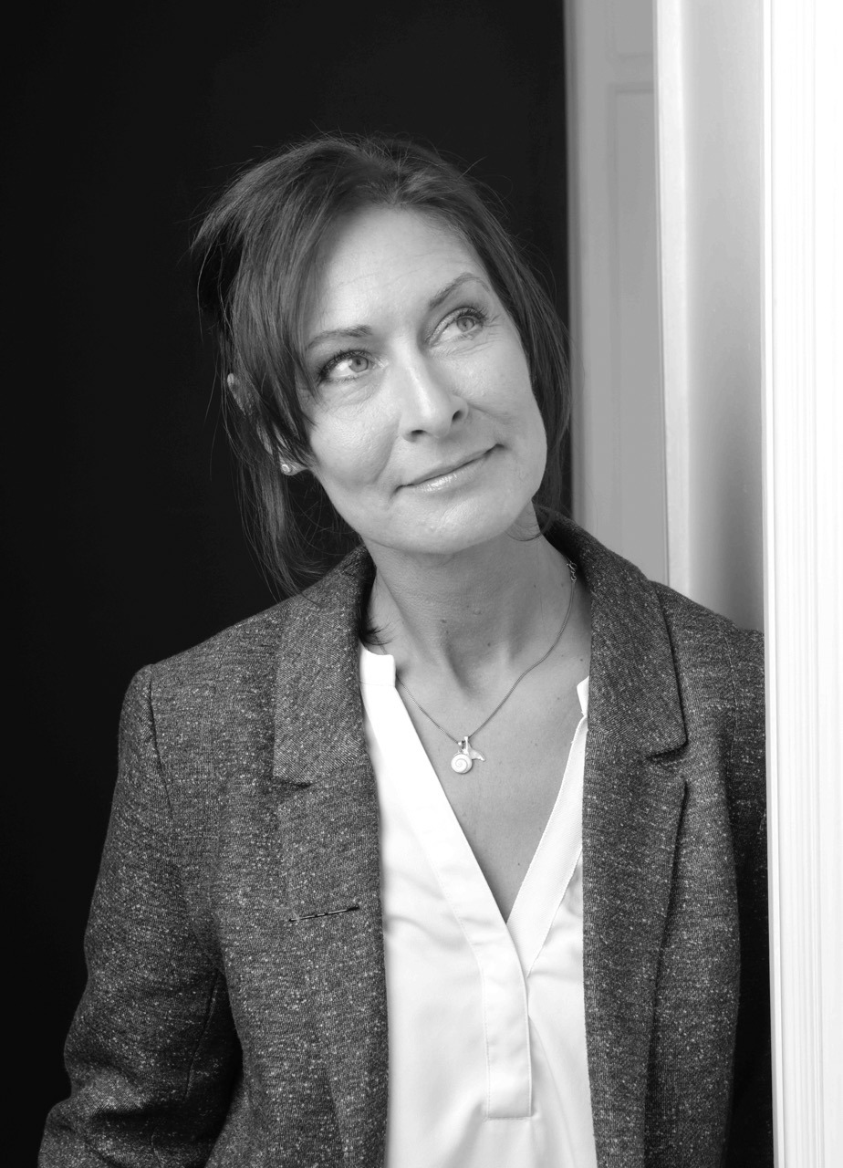 A professional black and white portrait of a woman in a grey blazer looking upwards thoughtfully.