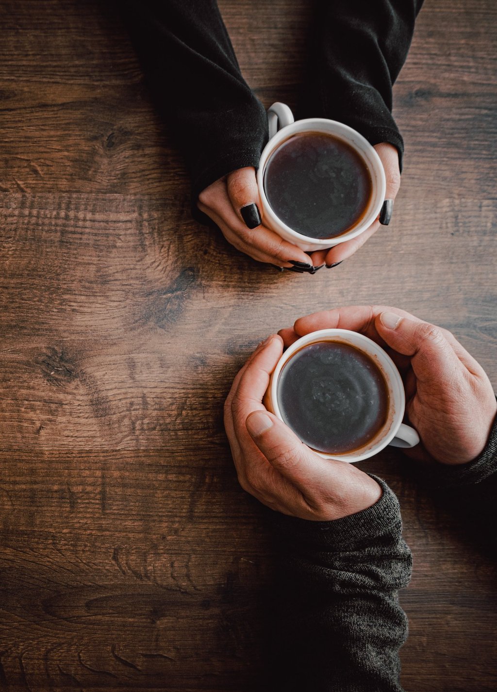 Two people holding cups of coffee meet to talk