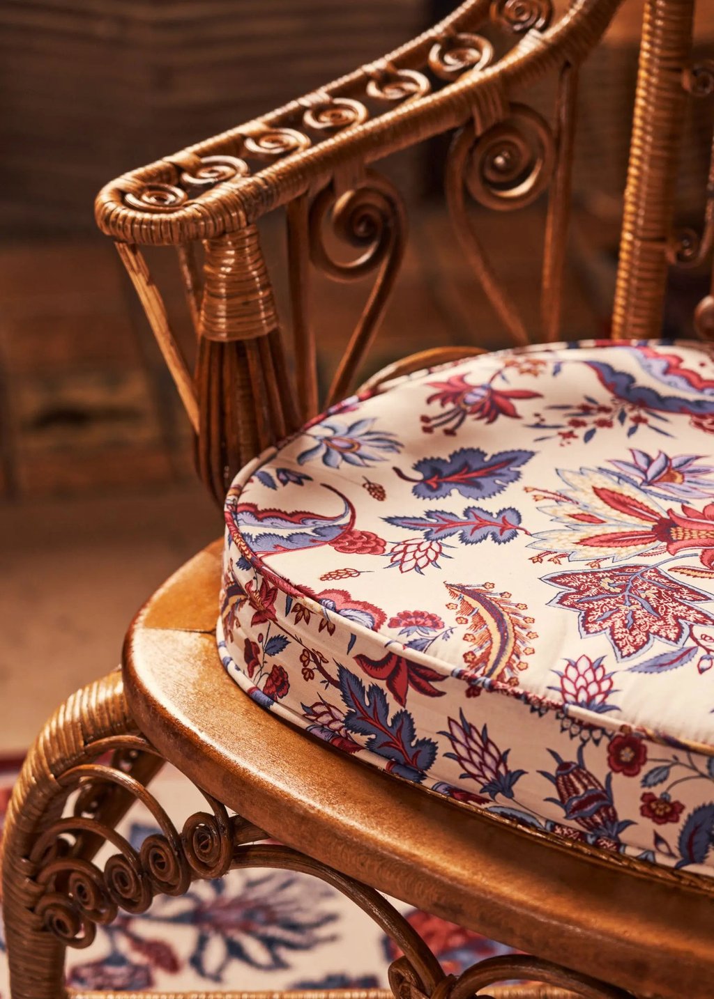 Fauteuil en osier avec posé dessus un coussin recouvert d'un tissu à motifs floraux