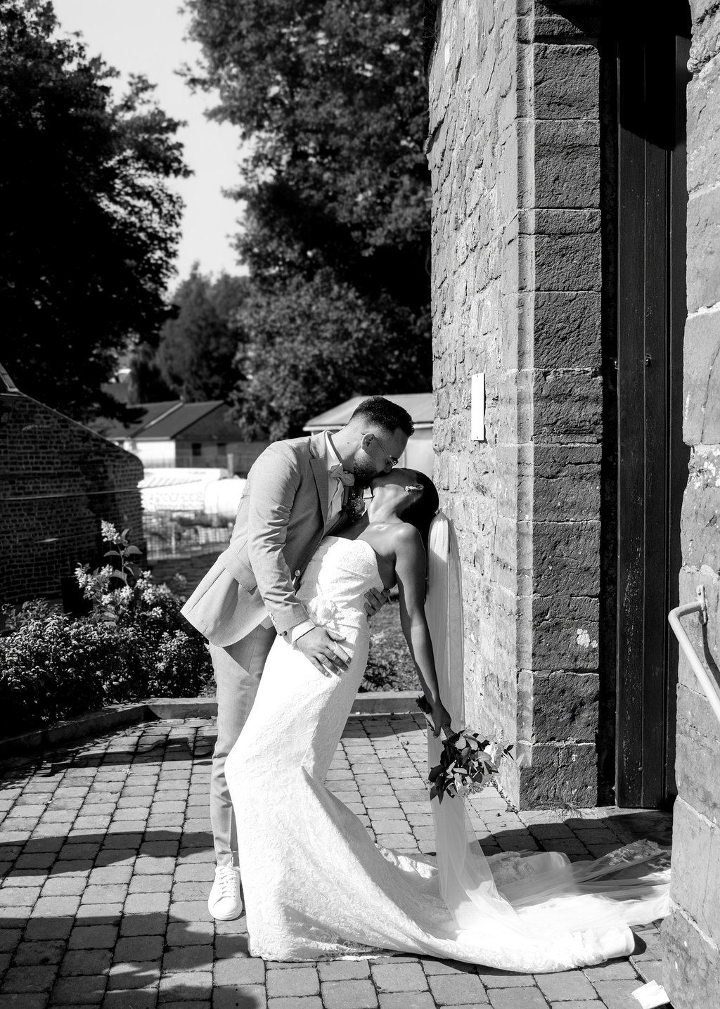 Photo en noir et blanc d'un marié embrassant sa femme devant une Église