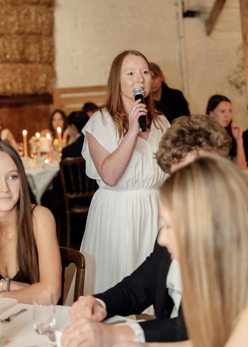 woman in white dress talking to the microphone during an event