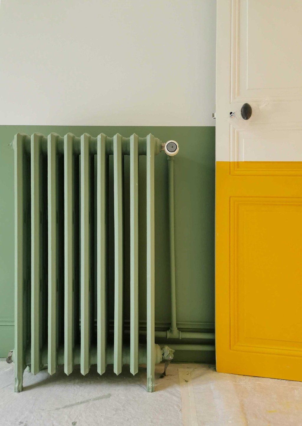 Vintage sage green radiator next to a yellow and white paneled door in a modern room.