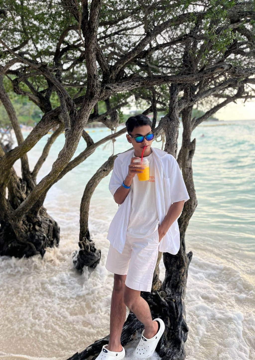 Male massage therapist leaning against a tree by the beach