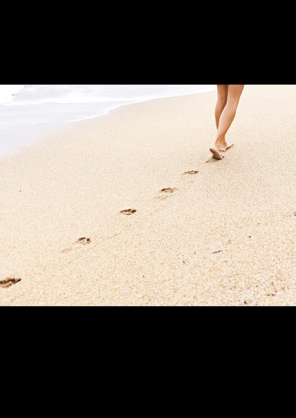 Voetafdrukken in zand op het strand bij de kustlijn.