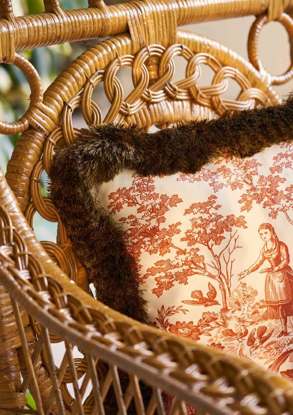 Fauteuil en osier avec posé dessus un coussin de toile de jouy et marabout rasé sur le tour