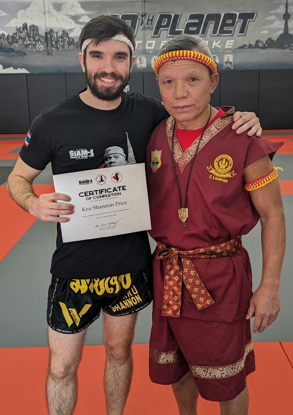 Kru Shannon stands next to Ajhan Suchart after recieving his Kru Certification.