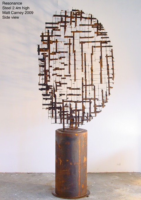 a rusted steel cross-hatched  circle sculpture on a rusted cylinder base side view