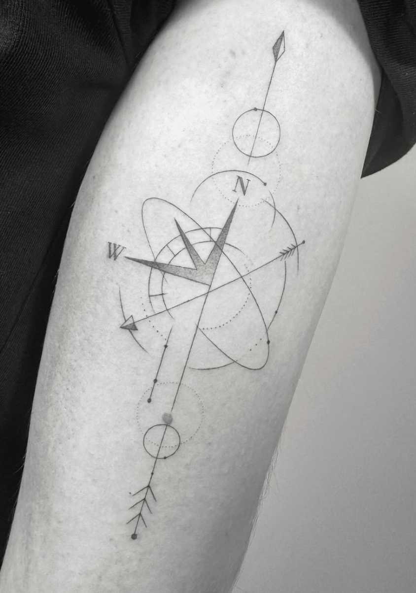Tatuaje fineline brújula geométrica con átomo y flechas en antebrazo madrid