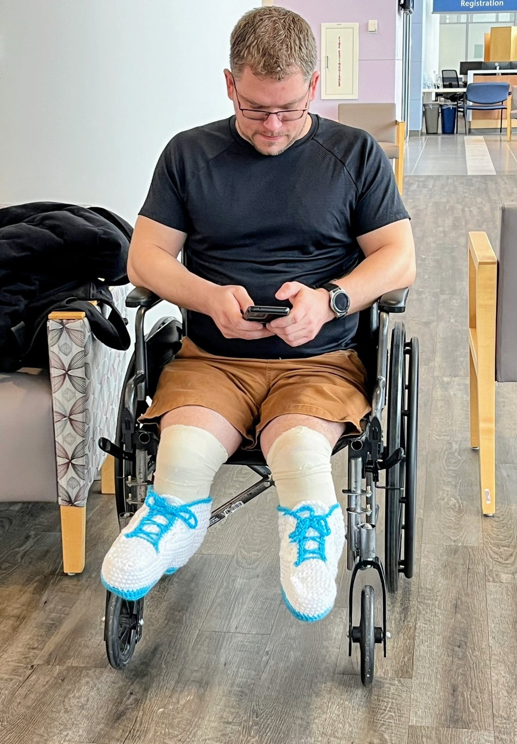 Person wearing handmade crocheted shoes sitting in a wheelchair at a doctor's office